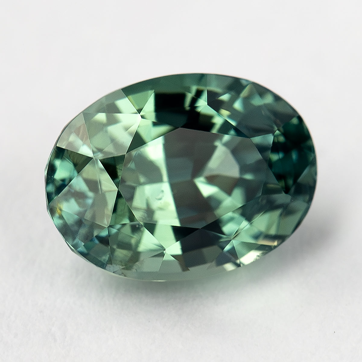 Teal-green oval sapphire turned diagonally, with a bright central facet reflection and darker edges.