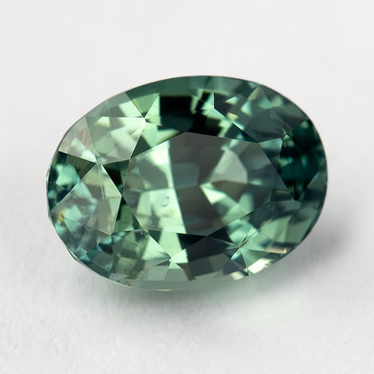 Teal-green oval sapphire turned diagonally, with a bright central facet reflection and darker edges.