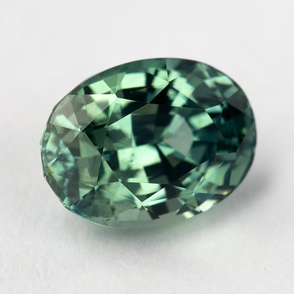 Angled face-up view of the teal-green oval sapphire, showing mixed green reflections across the crown.