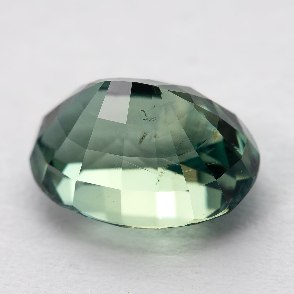 Low back-facing view of the teal-green oval sapphire, with pale reflections and visible internal detail.