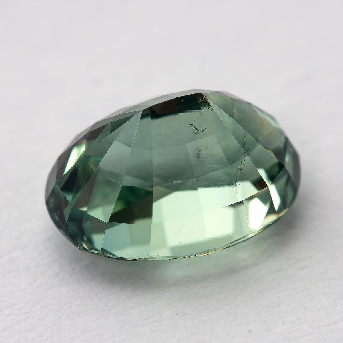 Diagonal back-facing macro of the teal-green oval sapphire, showing pavilion facets and internal detail.