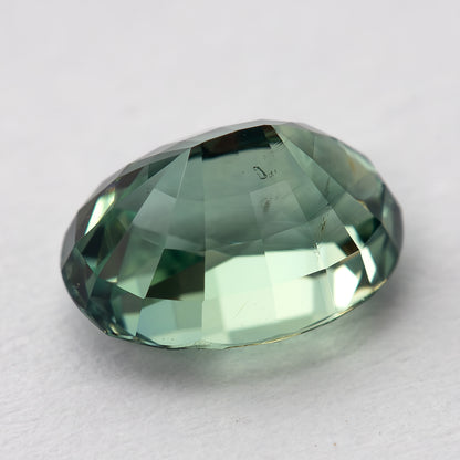 Diagonal back-facing macro of the teal-green oval sapphire, showing pavilion facets and internal detail.