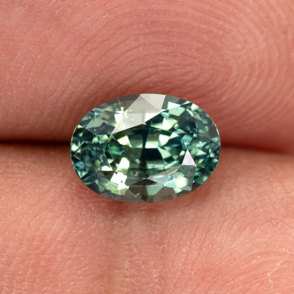 Teal-green oval sapphire on fingertips, with bright green and pale reflections across the crown.
