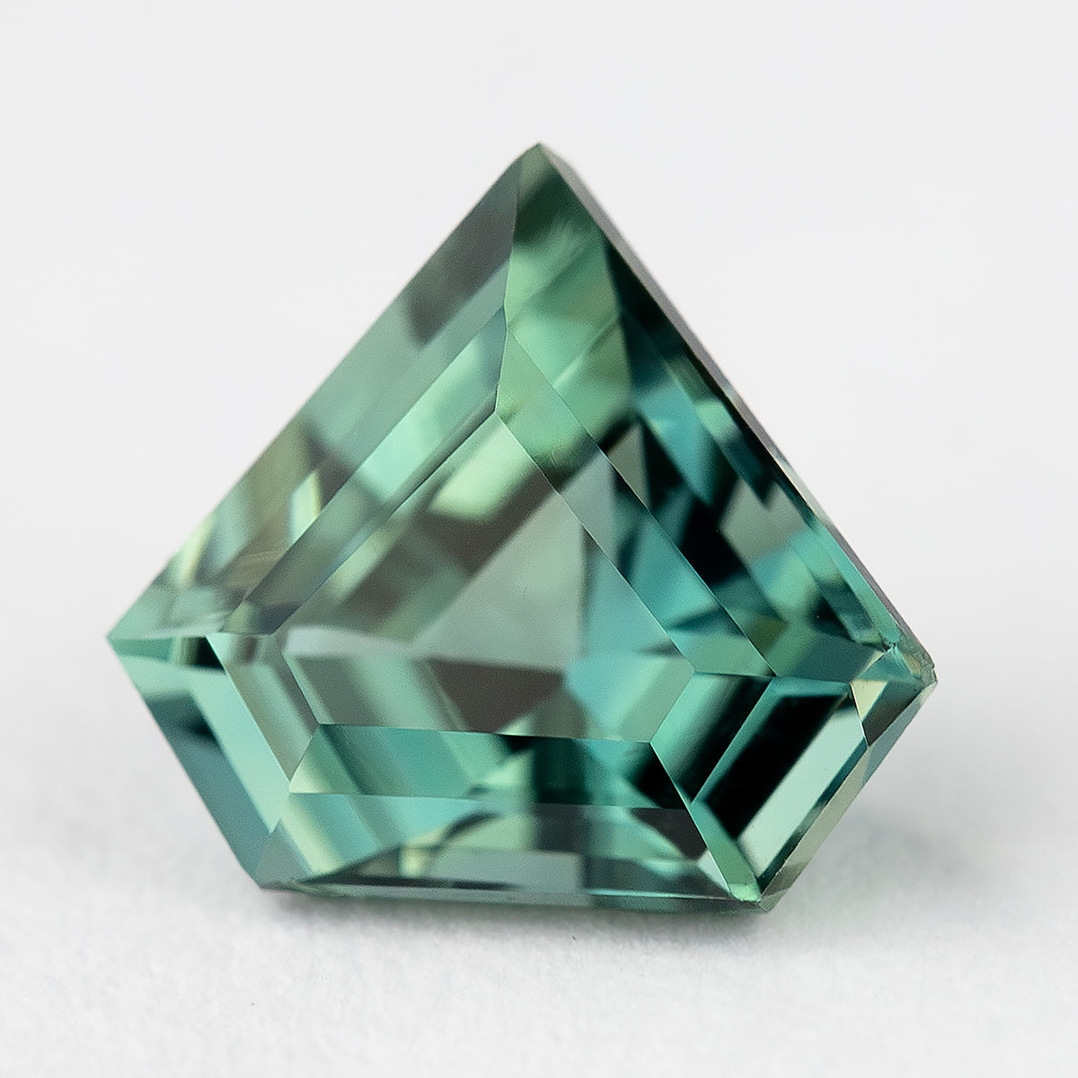 Face-up view of the exact teal-green shield-cut sapphire on a light background, showing its pointed outline and geometric facets.