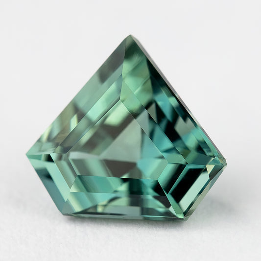 Face-up view of the exact teal-green shield-cut sapphire on a light background, showing its pointed outline and geometric facets.