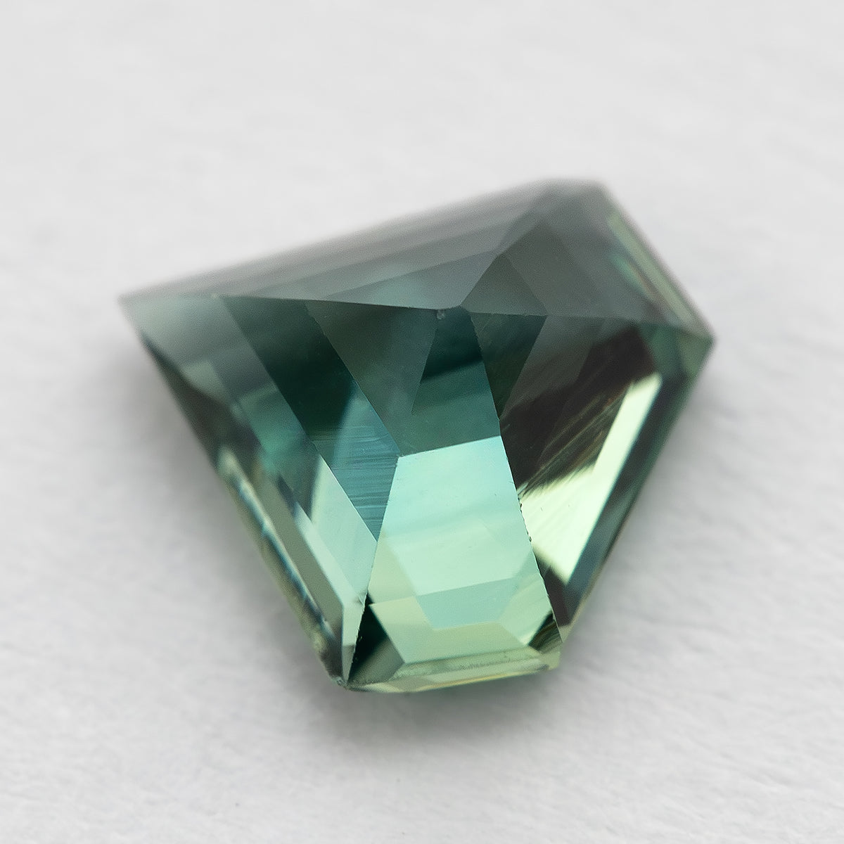Angled pavilion-side view of the sapphire resting on a light surface, showing its depth and back facets.