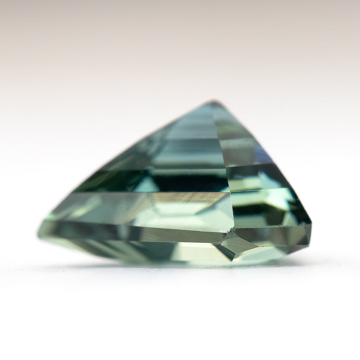 Side-profile view of the shield-cut sapphire on a light surface, showing its crown, girdle and pavilion depth.