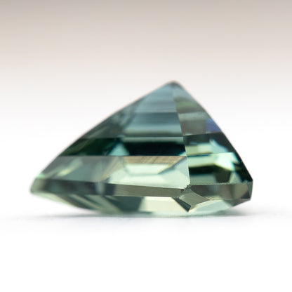 Side-profile view of the shield-cut sapphire on a light surface, showing its crown, girdle and pavilion depth.