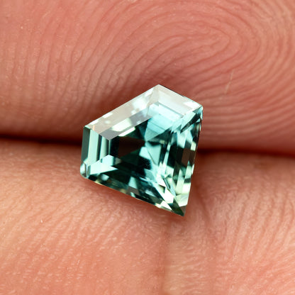 Low angled hand-scale view of the shield sapphire, showing its size and depth against a fingertip.