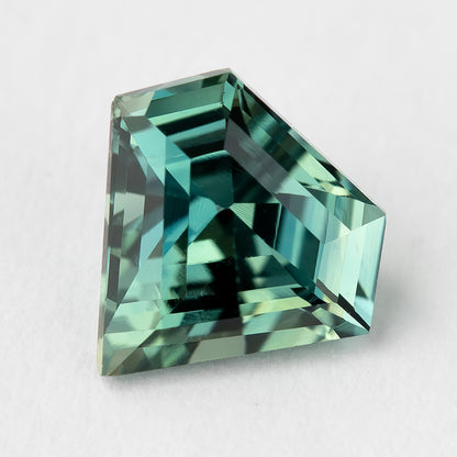 Tilted view of the sapphire on a light surface, showing the asymmetrical shield outline and stepped geometric reflections.