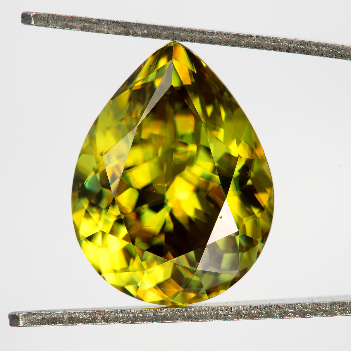 Green-yellow pear-shaped sphene held face-up upright in tweezers, showing yellow, green and dark facet reflections.
