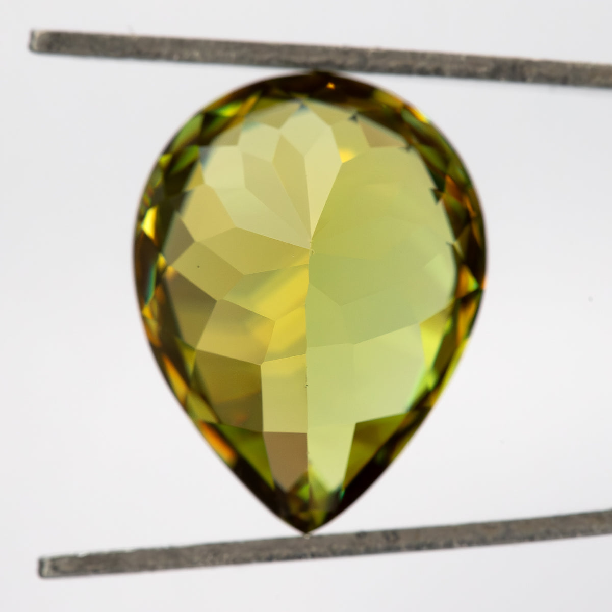 Pavilion-side view of the pear-shaped sphene in tweezers, showing broad pale-yellow facets.