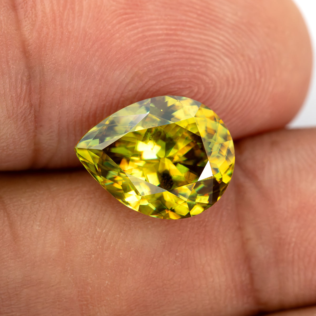 Wider fingertip view of the green-yellow pear-shaped sphene showing its size relative to the fingers.