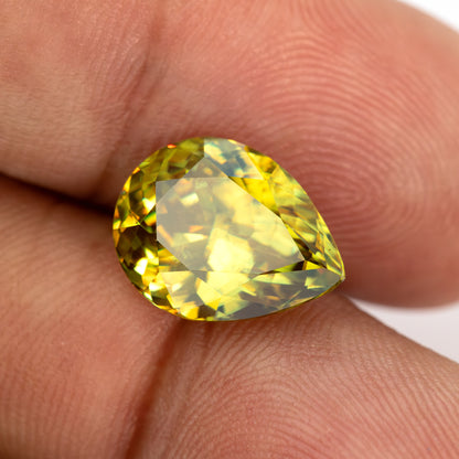 Pear-shaped sphene tilted face-up on fingertips with a broad light reflection across the centre.