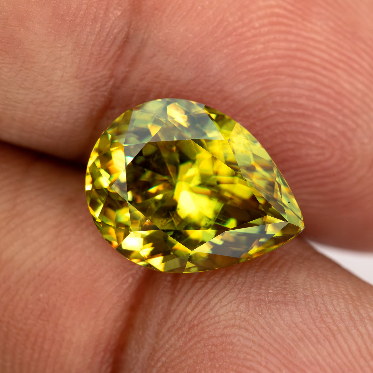 Green-yellow pear-shaped sphene on fingertips with bright yellow reflections across the face.