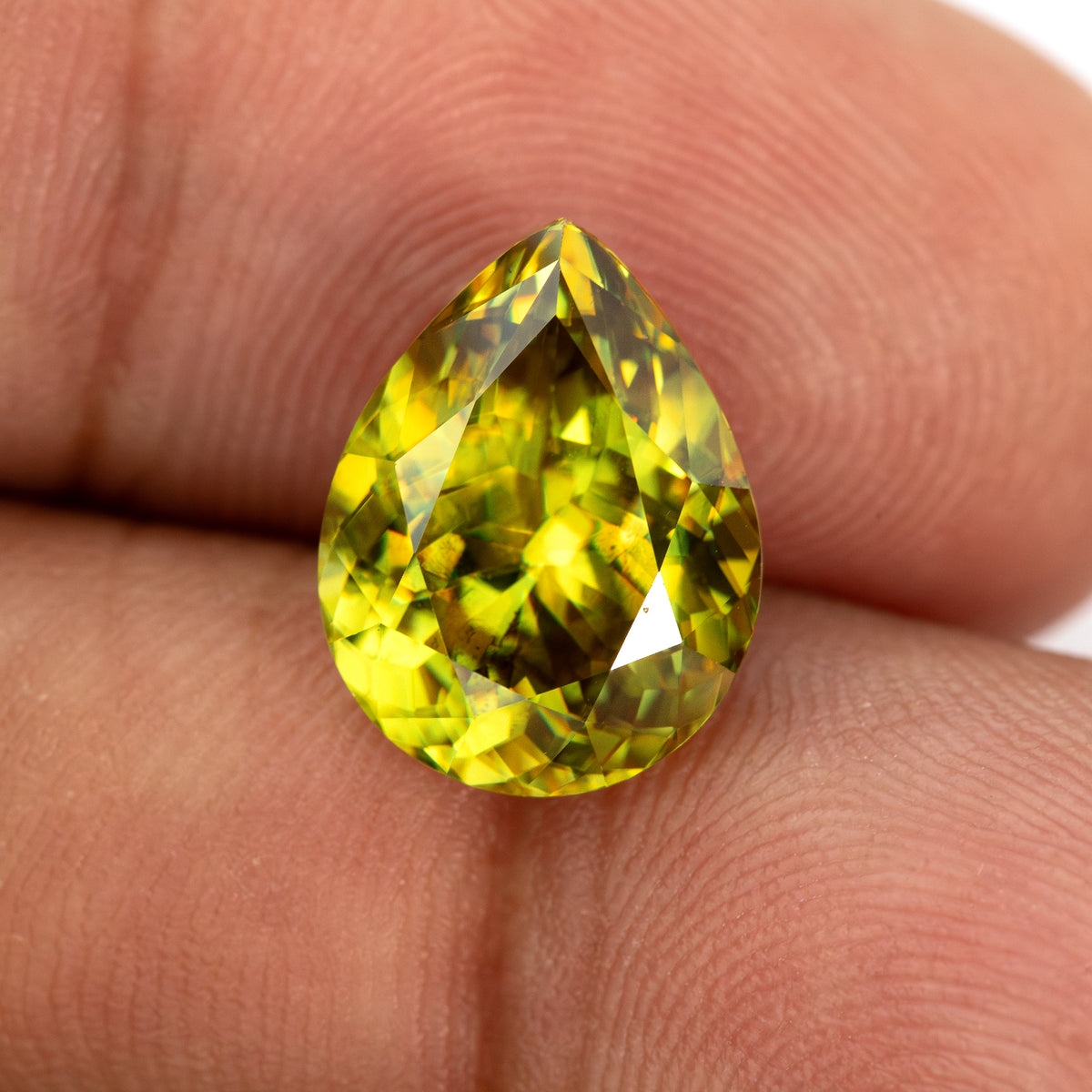 Pear-shaped sphene held upright face-up against a finger, showing its rounded base and pointed tip.