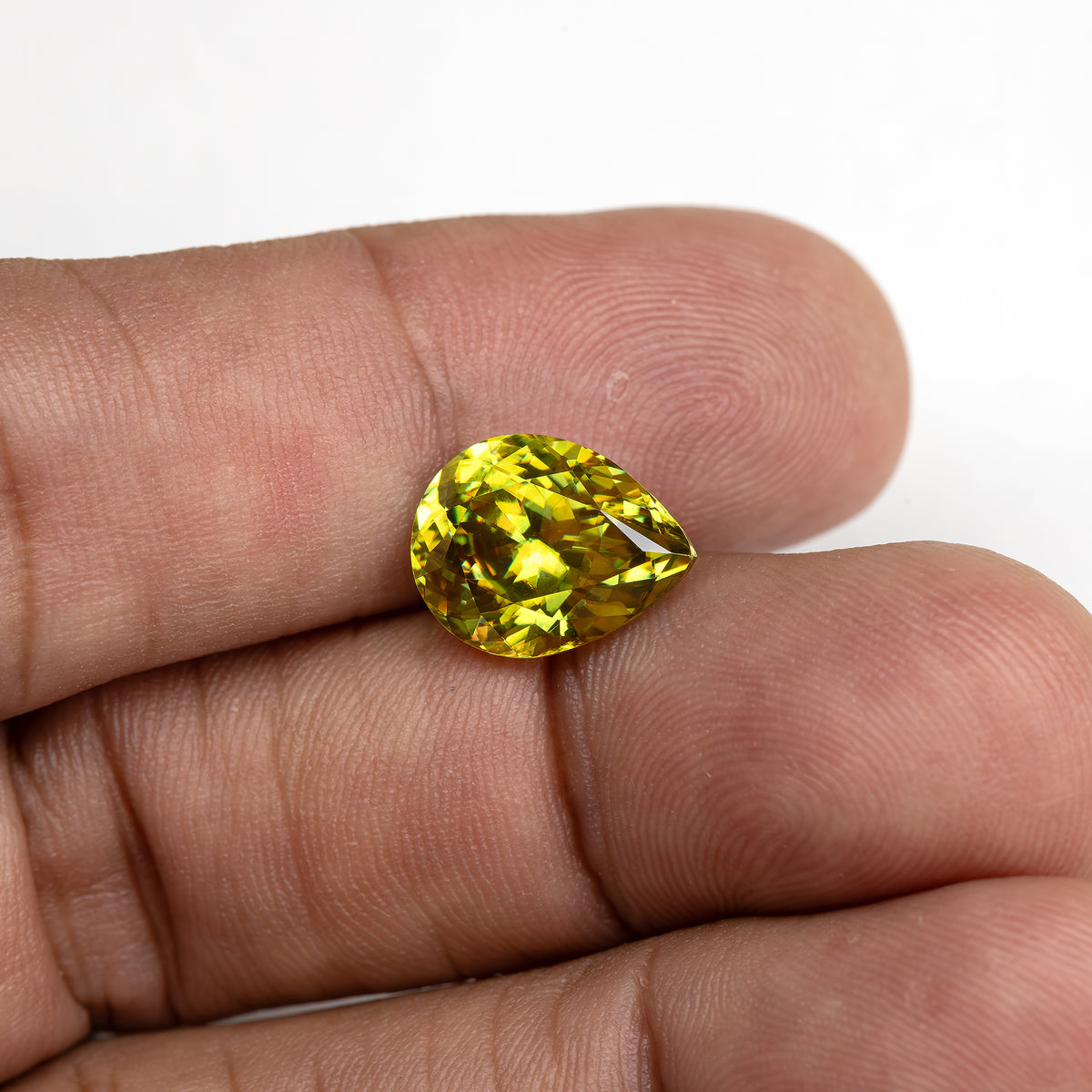 Wider hand view of the green-yellow pear-shaped sphene resting on fingertips for scale.