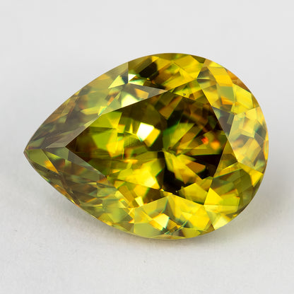 Green-yellow pear-shaped sphene resting face-up horizontally on white, with distinct yellow and dark crown facets.