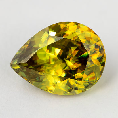 Green-yellow sphene viewed face-up at an angle on white, showing golden and darker facet reflections.