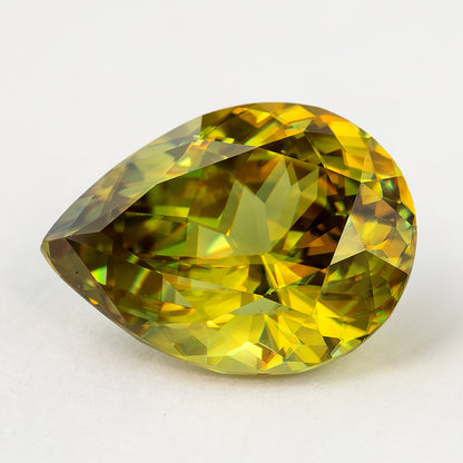 Low angled face-up view of the green-yellow pear-shaped sphene on a white surface.