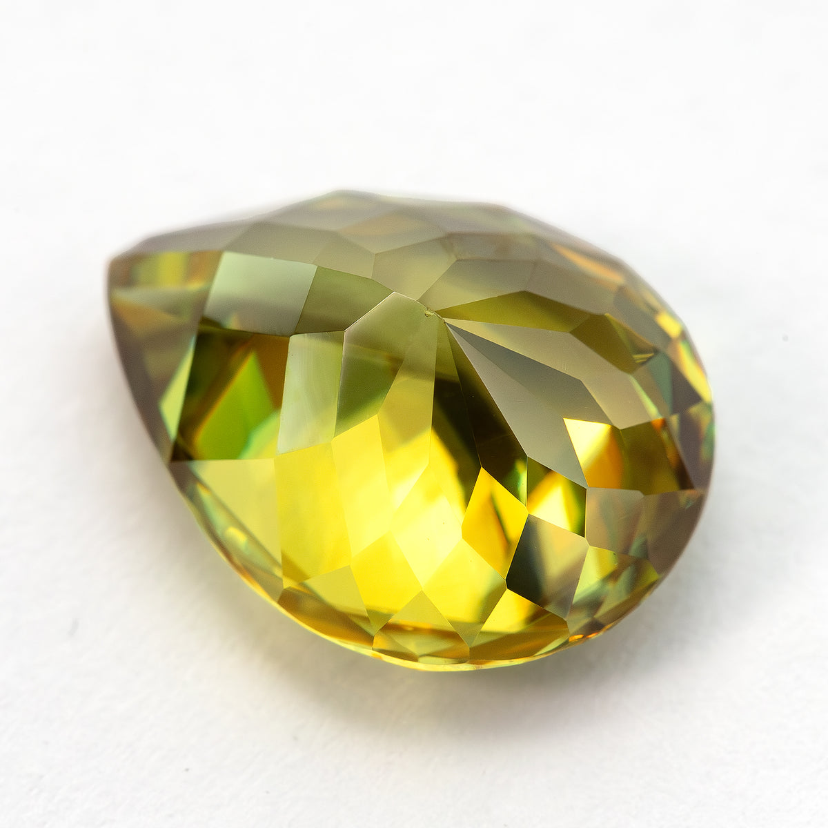 Low angled pavilion-side view of the pear-shaped sphene on white, showing yellow reflections.