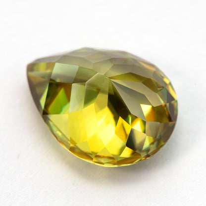 Low angled pavilion-side view of the pear-shaped sphene on white, showing yellow reflections.