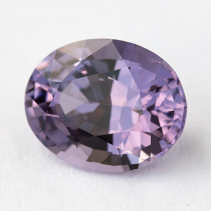 Oval lavender-pink spinel on a pale surface showing its table from an alternate angle.
