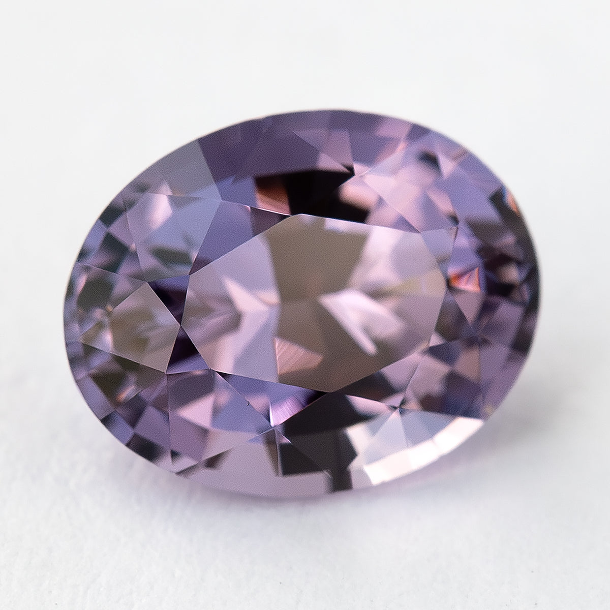 Face-up oval spinel on a pale surface with pink and purple reflections.