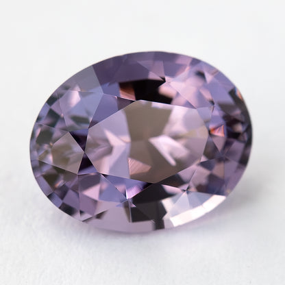 Face-up oval spinel on a pale surface with pink and purple reflections.