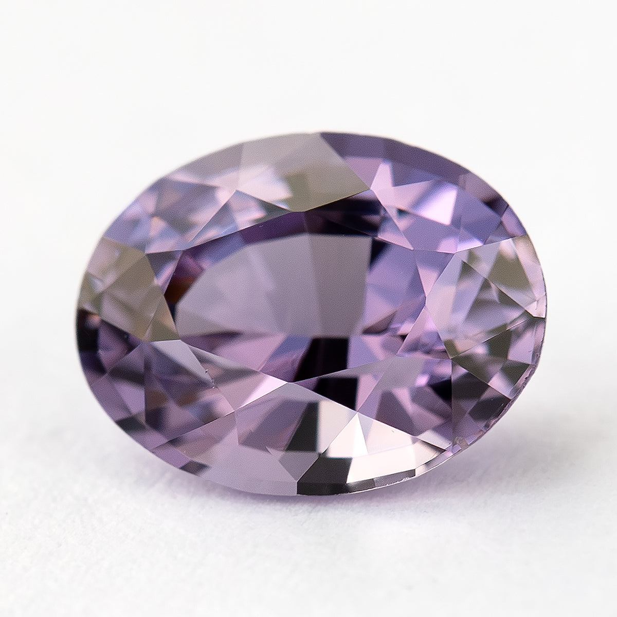 Alternate face-up view of lavender-pink oval spinel on a pale surface.
