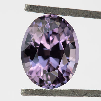 Lavender-pink oval spinel held face-up vertically in tweezers.