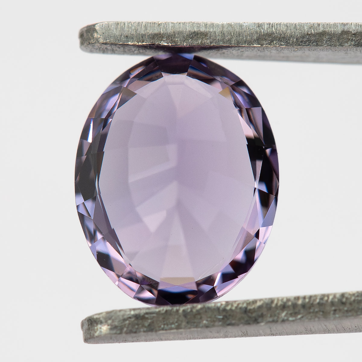 Reverse view of oval spinel held in tweezers against a pale background.