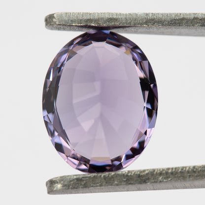 Reverse view of oval spinel held in tweezers against a pale background.