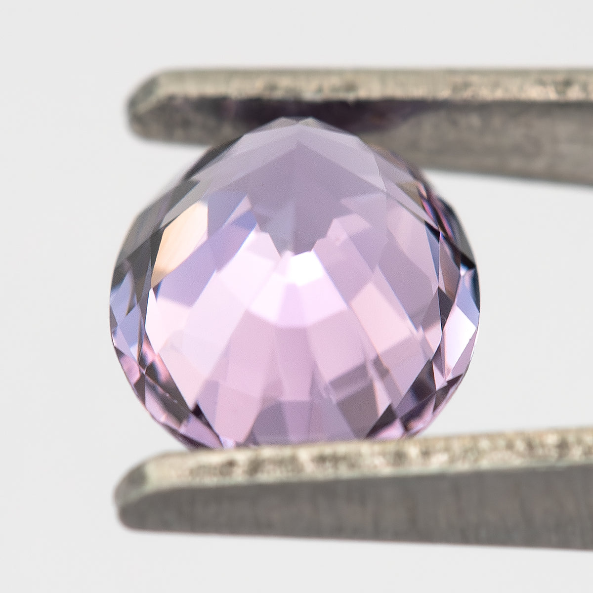Oblique pavilion view of lavender-pink spinel held in tweezers.