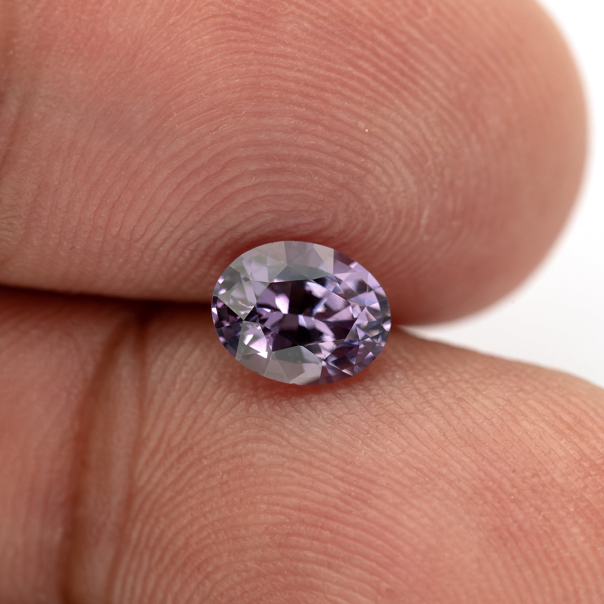 Oval spinel resting face-up between fingertips for scale.