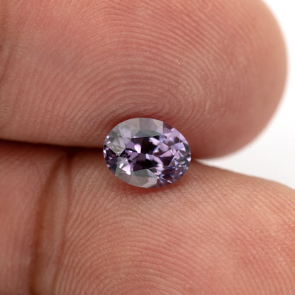 Oval spinel resting face-up between fingertips for scale.