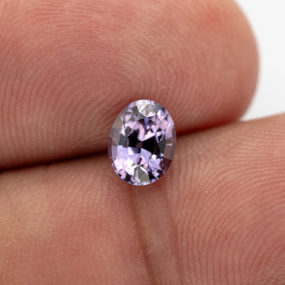 Lavender-pink oval spinel resting vertically between fingertips, showing its face-up outline.