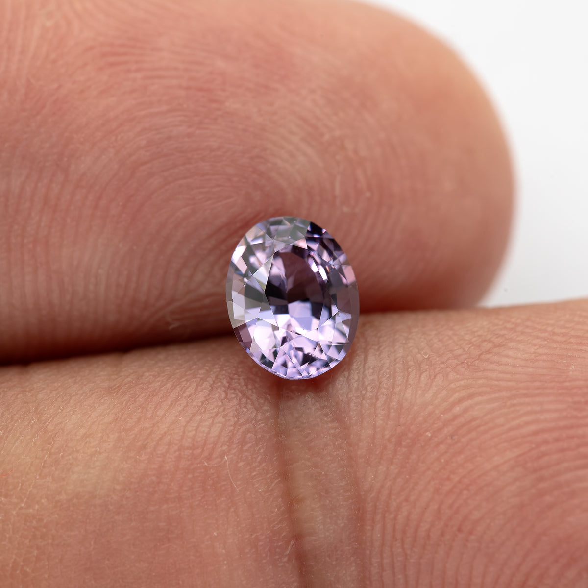 Face-up oval spinel between fingertips from an alternate angle.