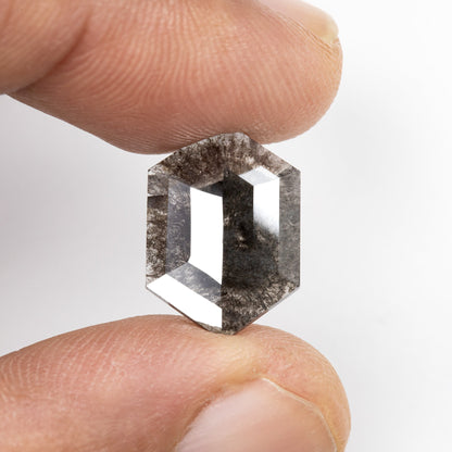 Gray hexagonal diamond held between fingers, showing its size and bright rose-cut facets.
