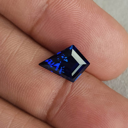 Royal blue kite sapphire lying sideways across fingertips, with a bright pale reflection along one edge.