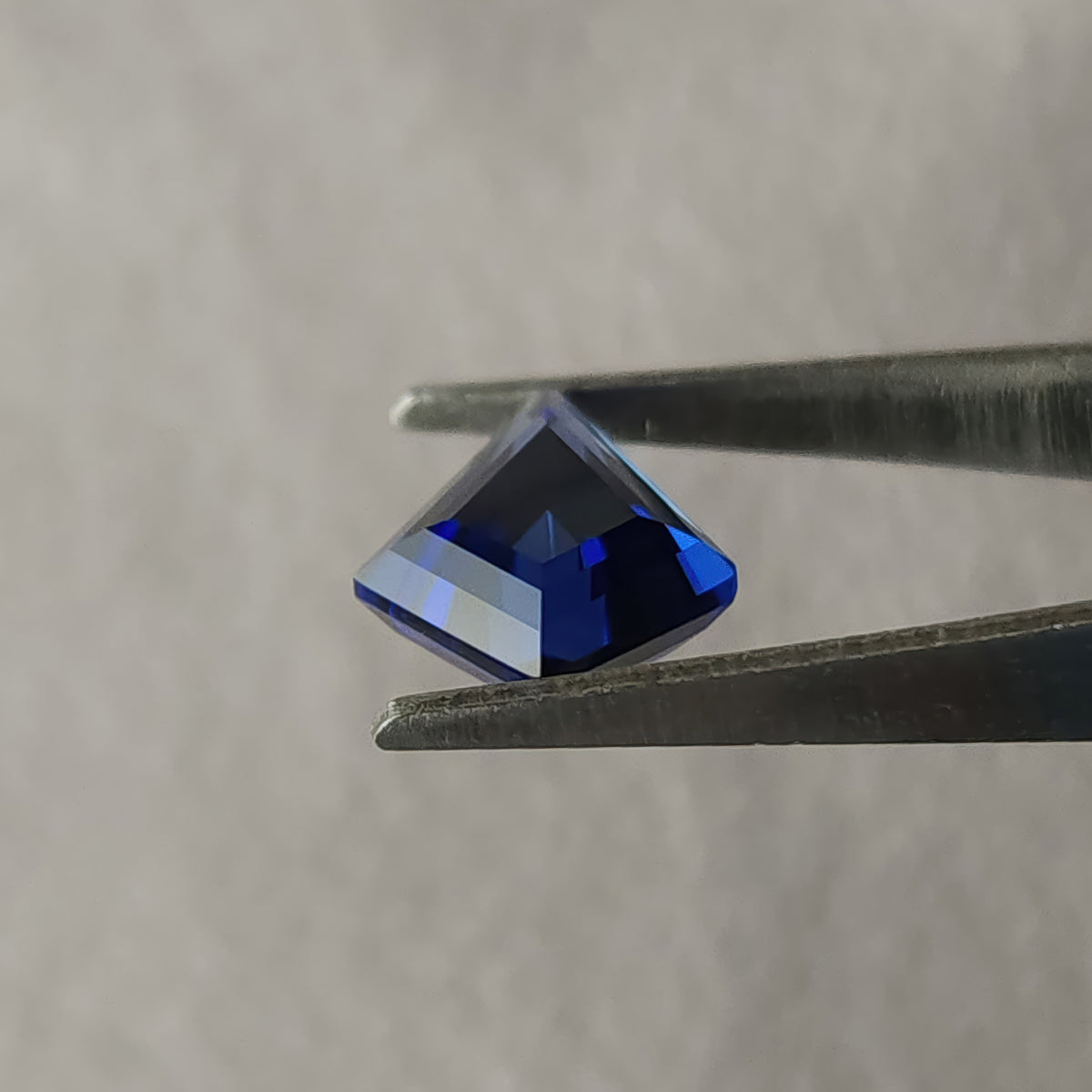 Side profile of the blue kite sapphire in tweezers, showing its crown and pointed pavilion beneath the girdle.