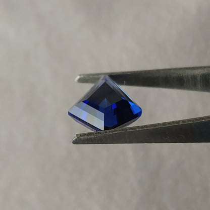 Side profile of the blue kite sapphire in tweezers, showing its crown and pointed pavilion beneath the girdle.