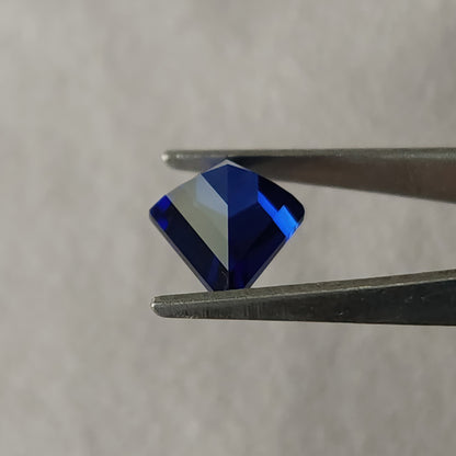 Angled pavilion of the royal blue kite sapphire in tweezers, with broad blue and pale reflected planes.