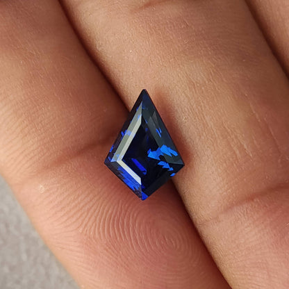 Single royal blue kite sapphire on fingers, with the long point upright and bright blue facets across the crown.