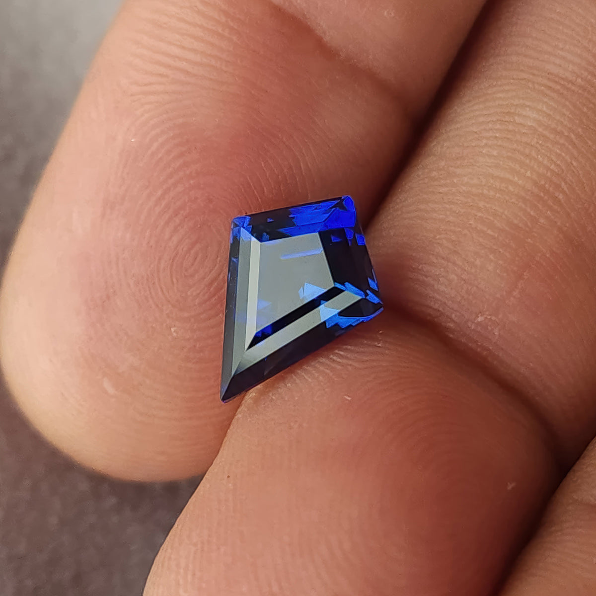 Blue kite sapphire tilted across fingers, showing a broad pale central reflection and sloping crown edges.