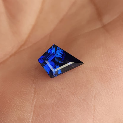 Kite-cut lab-grown sapphire lying sideways in a palm, showing a long dark point and bright blue crown reflections.