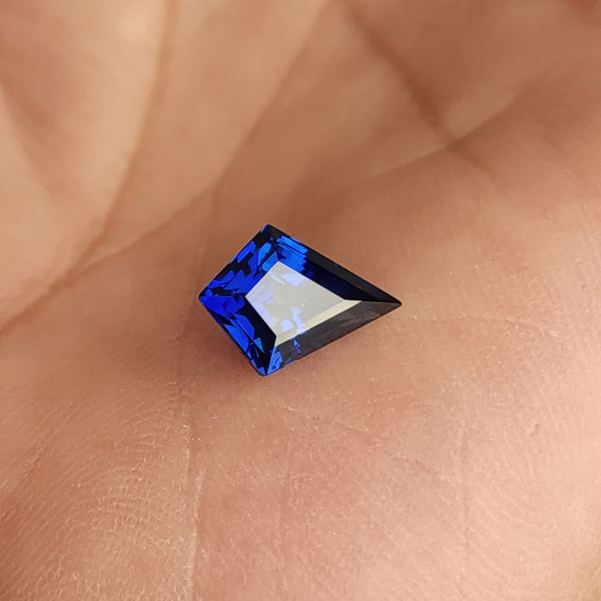 Blue kite sapphire on a palm at a pale-reflecting angle, showing the pointed outline and hand for scale.