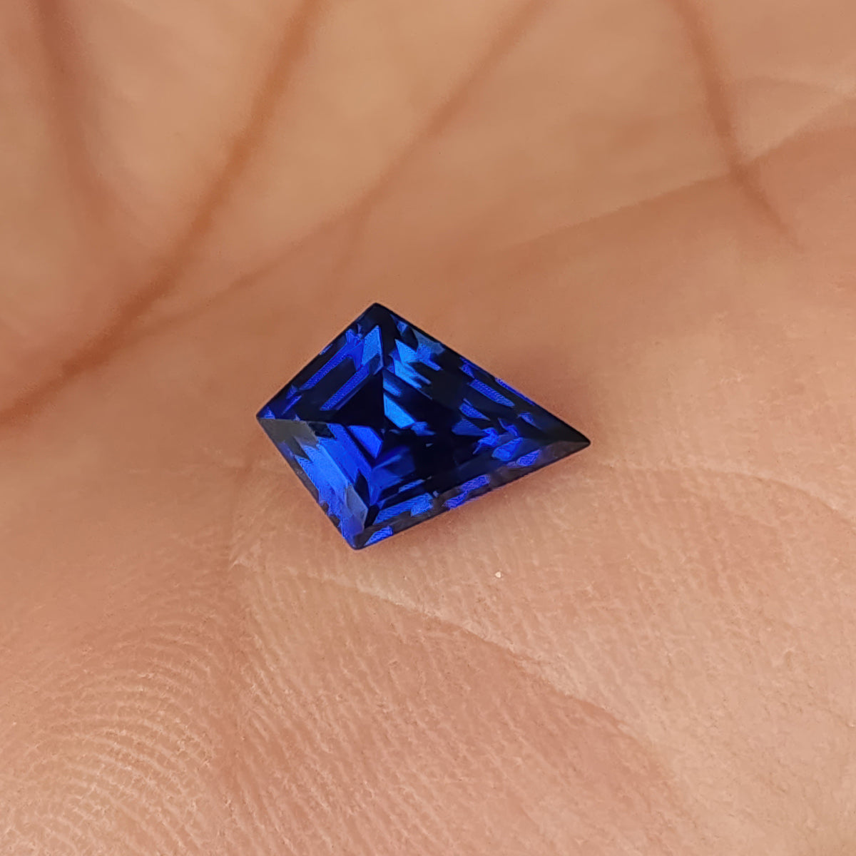 Royal blue kite sapphire on a palm with its short edge upward, showing a strong blue geometric facet pattern.