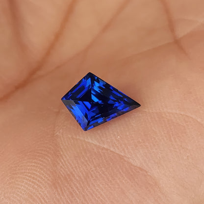 Royal blue kite sapphire on a palm with its short edge upward, showing a strong blue geometric facet pattern.