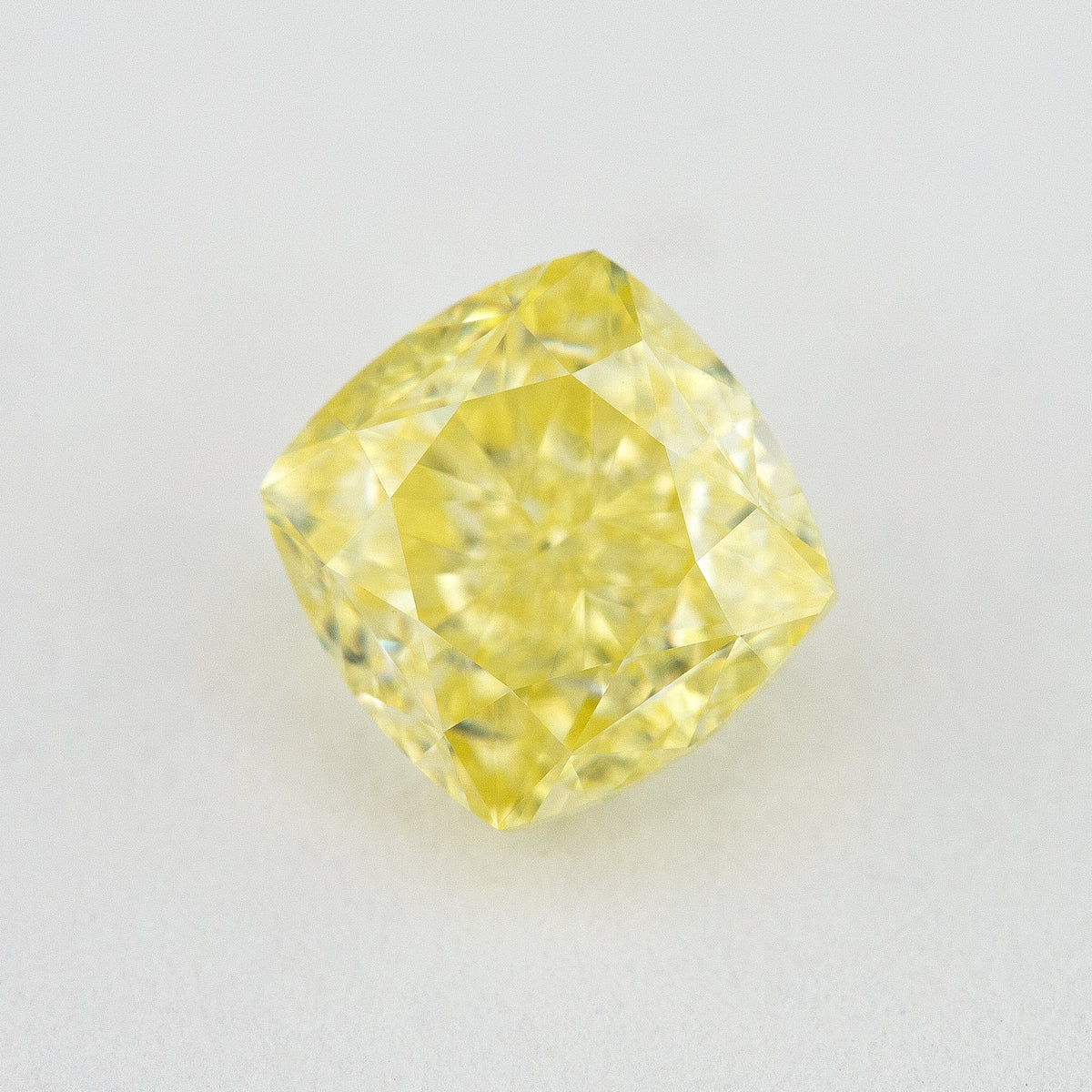 Face-up cushion-shaped yellow diamond on a pale surface, showing its complete outline, table and crown facets.